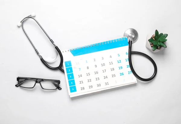 Calendar with a stethoscope on a gray background. Scheduled medical examination