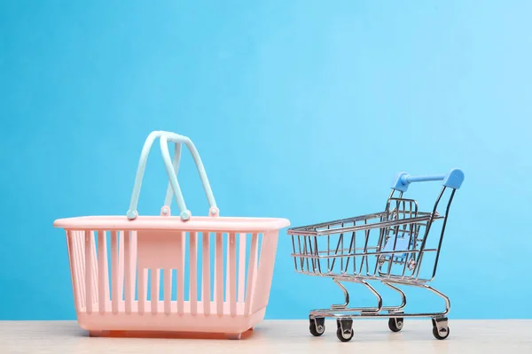Miniature mini supermarket basket and trolley on the table, blue background. Shopping concept