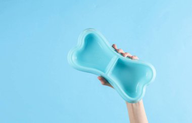 Mavi arka planda köpek kemiği şeklinde bir tabağı tutan el.