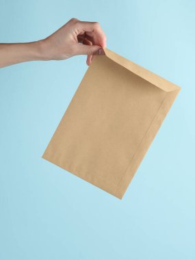 Kraft posta zarfında mavi arka planda bir kadın eli var.