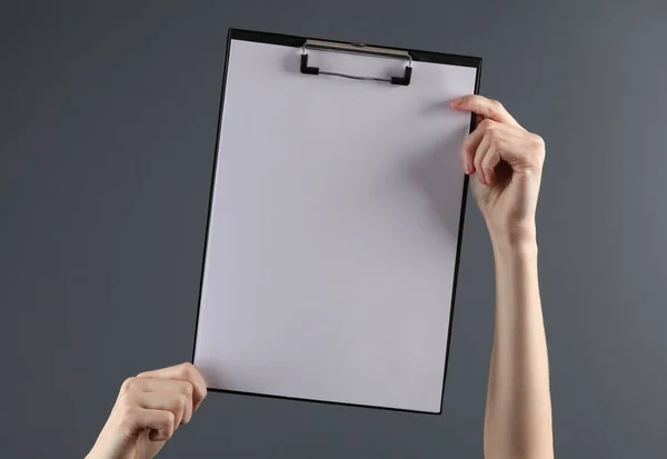Female hands holding a clipboard with an empty white sheet on a dark background