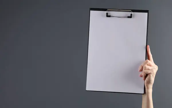 Female hand holding a clipboard with an empty white sheet on a dark background