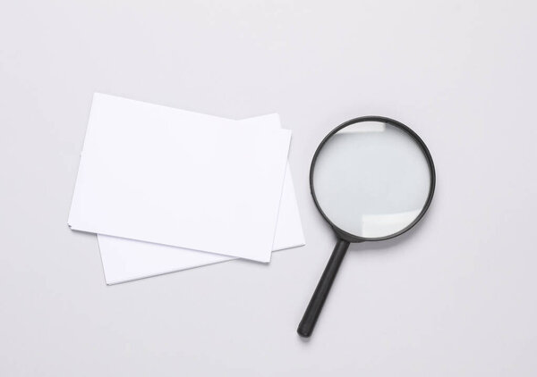 White blank sheets of paper with magnifying glass on gray background. Creative layout, mockup, template for design