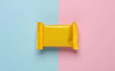 Mavi-pembe pastel arka planda sarı şeker paketi. Üst görünüm