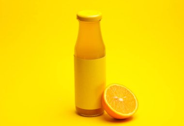 Sarı arka planda yarım portakal suyu olan bir şişe portakal suyu.