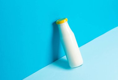 Mavi arka planda cam bir şişe yoğurt.