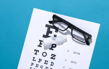 Göz testi çizelgesi ve mavi arka planda göz damlası olan gözlükler. Görüş kontrolü, düzeltme
