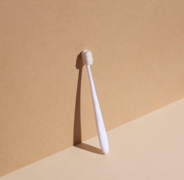 Beyaz diş fırçası, bej-kahverengi arka planda, gölgeli. Minimalist kompozisyon. Yaratıcı yerleşim