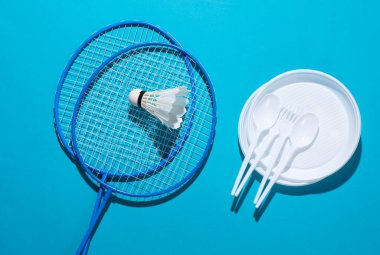 Piknik. Badminton raketi. Mekik sikli ve plastik plakalı. Mavi arka planda kaşıklar ve çatallar.