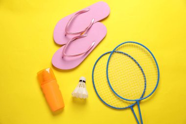 Plaj tatili Badbinton raketi, pipi, parmak arası terlik, sarı arka planda gölgeli güneş kremi. Düz yatıyordu