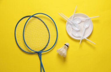 Piknik. Badminton raketi. Mekik sikli ve plastik plakalı. Sarı arka planda kaşıklar ve çatallar.