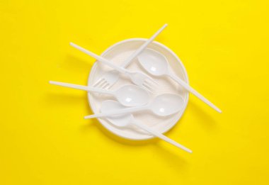 Plastik kaşıklar ve çatallar sarı arka planda bir tabakta.