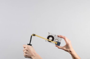 Gri arkaplanda ses kaseti olan sapanı tutan eller.