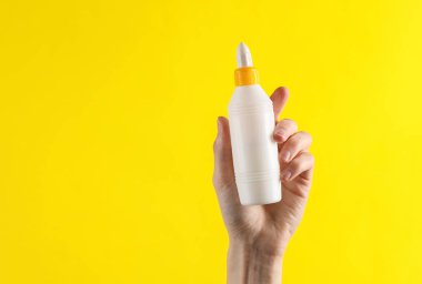 Sarı arka planda tutkal şişesi tutan kadın.