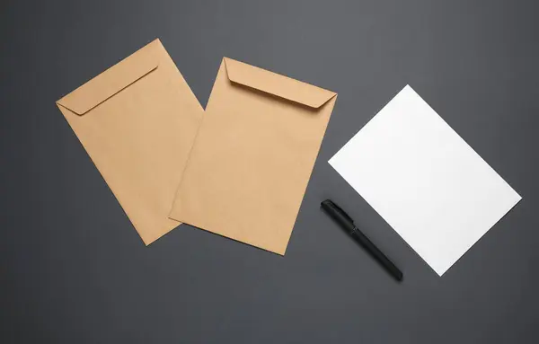 Craft postal envelopes with white blank letter, pen on a gray background