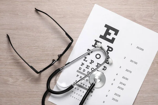 Eyeglasses with stethoscope and eye test chart on table. Vision examination and correction. Top view