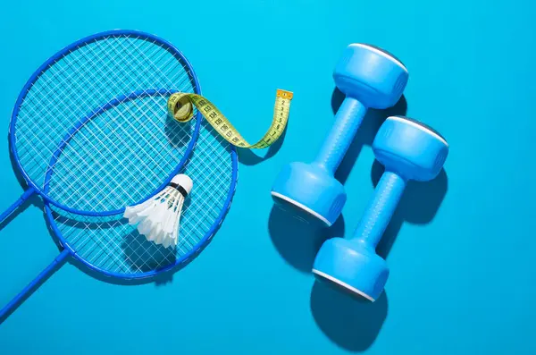 Weight loss, slimming, fitness and outdoor activities. Badminton racket with shuttlecock and dumbbells on a blue background. Flat lay