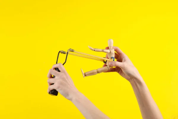 Hands holding slingshot with wooden puppet on a yellow background. Business concept