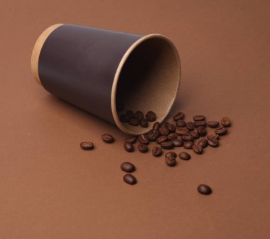 Kahverengi arka planda kahve çekirdekleri olan tek kullanımlık karton bardak.