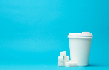 Tek kullanımlık beyaz karton bardak ve mavi arka planda şeker küpleri. Boşluğu kopyala