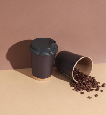 Kahverengi arka planda kahve çekirdekleri olan tek kullanımlık karton bardak. Yaratıcı yerleşim