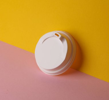 Sarı-pembe arka planda tek kullanımlık beyaz plastik bardak kapağı. Model, tasarım şablonu