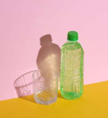 Plastik su şişesi ve pembe-sarı arka planda gölgeli cam. Yaratıcı yerleşim
