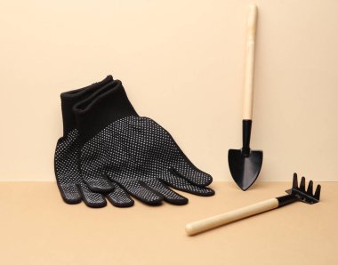 Minyatür bahçe aletleri seti (tırmıklar, kürekler) ve kahverengi bej arka planda çalışan eldivenler. Yaratıcı yerleşim