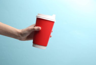 Kırmızı kullan-at bardakla el ele tutuşup mavi arka planda sıcak içecek (çay, kahve) alın.