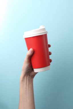 Kırmızı kullan-at bardakla el ele tutuşup mavi arka planda sıcak içecek (çay, kahve) alın.