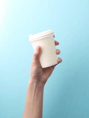 El ele tutuşan beyaz kullan-at bardaklar. Sıcak içecekler için. Mavi arka planda çay, kahve.