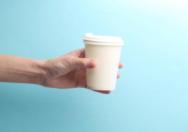 El ele tutuşan beyaz kullan-at bardaklar. Sıcak içecekler için. Mavi arka planda çay, kahve.