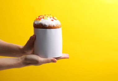 Sarı arka planda beyaz etiketli Paskalya pastası tutan eller.