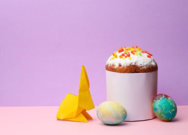 Beyaz etiketli Paskalya pastası ve pastel arka planda origami tavşanlı renkli yumurtalar. Paskalya 'da hayat