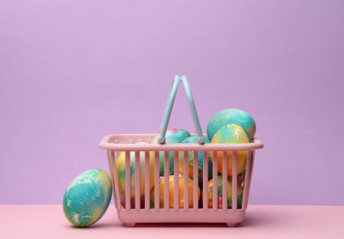 Pastel arka planda Paskalya yumurtaları olan süpermarket sepeti. Minimalizm Paskalyası