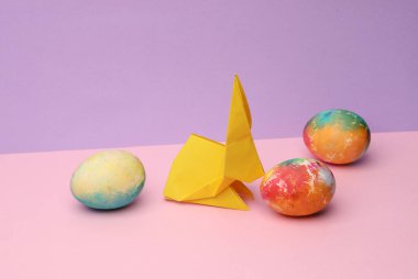 Pastel arka planda renkli yumurtaları olan Origami tavşanı. Kavramsal Paskalya fotoğrafı