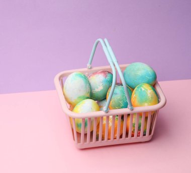 Pastel arka planda Paskalya yumurtaları olan süpermarket sepeti. Minimalizm Paskalyası