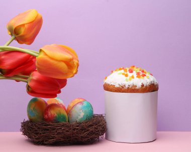 Yuvasında renkli yumurtalar ve pastel arka planda laleler olan Paskalya pastası. Paskalya 'da hayat