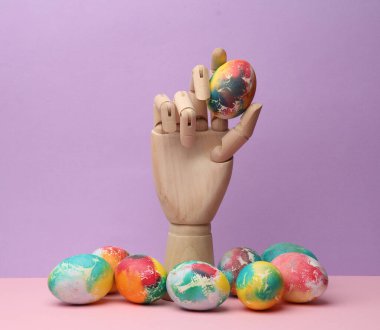 Ahşap el pastel arka planda renkli bir Paskalya yumurtası tutuyor. Asgari Paskalya natürmortu
