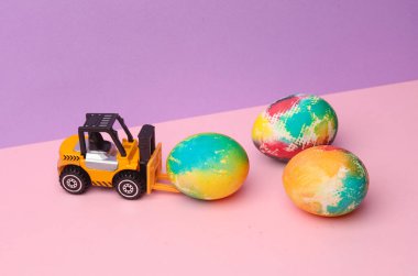 Pastel renkli arka planda Paskalya yumurtası olan oyuncak forklift. Minimalizm Paskalyası