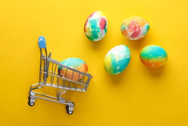 Pastel arka planda Paskalya yumurtası olan süpermarket arabası. Minimalizm Paskalyası