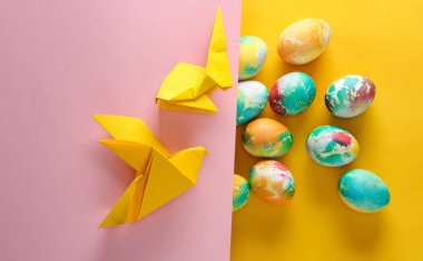 Çok renkli Paskalya yumurtaları, origami güvercini ve sarı arka planda bir tavşan..