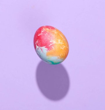 Çok renkli Paskalya yumurtası mor bir arka planda, gölgesi ile havada süzülüyor.