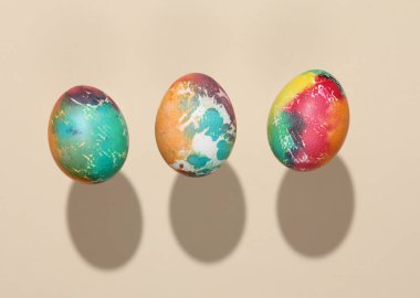 Renkli Paskalya yumurtaları bej arka planda, gölgeli havada süzülüyor.