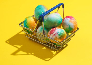 Sarı arka planda Paskalya yumurtaları olan süpermarket sepeti. Minimalizm Paskalyası