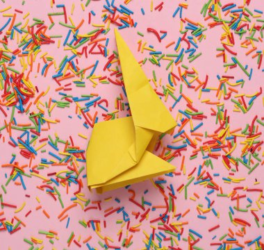 Renkli paskalya şekeri ya da pembe arka planda origami tavşanlı kek süslemesi.