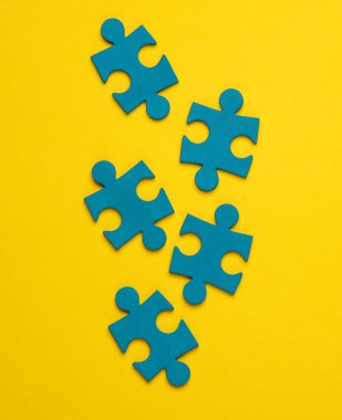 Sarı arkaplandaki mavi yapboz parçacıkları. İş konsepti