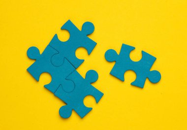 Sarı arkaplandaki mavi yapboz parçacıkları. İş konsepti