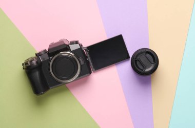 Kapaklı ekran ve pastel arka planda lens olan modern dijital kamera. Fotoğrafçı ekipmanı. Üst Manzara. Düz yatıyordu
