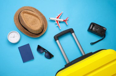 Sarı bavul, mavi arka planda seyahat aksesuarları olan bavul. Yaz tatili, seyahat, gezi konsepti. Üst Manzara. Düz yatıyordu